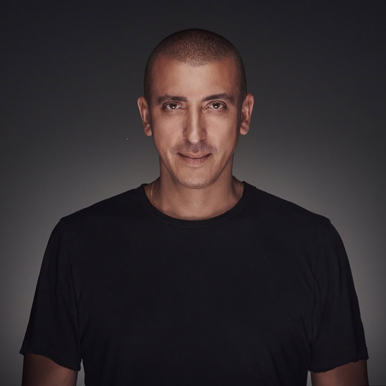 Porträt eines Mannes mit kurzem, glattem Haar und einem neutralen Gesichtsausdruck, der ein schwarzes T-Shirt trägt.