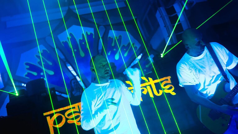 Zwei Künstler auf einer Bühne mit Laserlichtern und einem Hintergrund, der das Logo von Psy-Spirits zeigt.