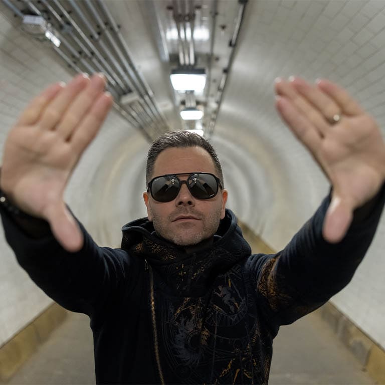 Mann in einem Tunnel, der mit seinen Händen eine Kamera-ähnliche Geste macht und Sonnenbrille trägt.