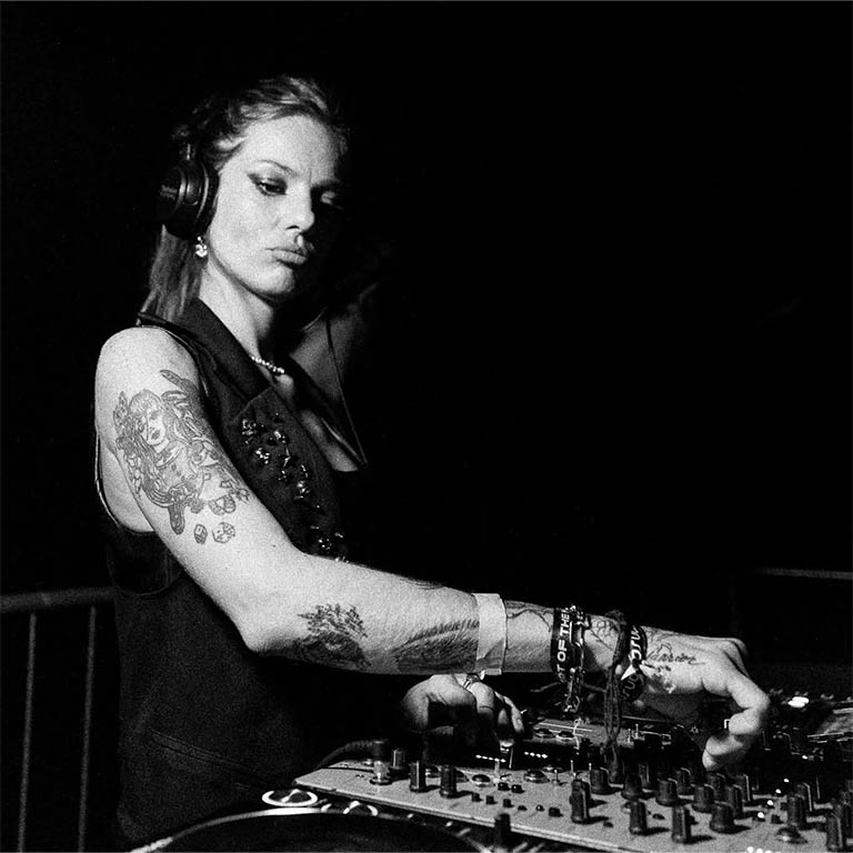 DJ mit Tätowierungen, die an einem Mischpult arbeitet und Kopfhörer trägt.
