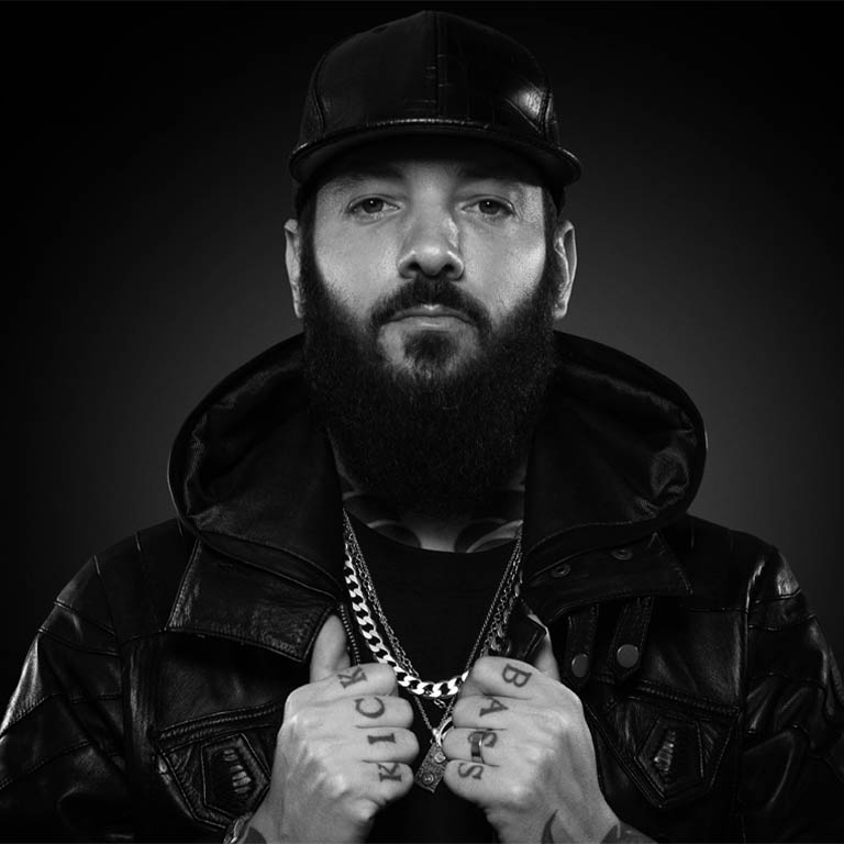 Mann mit Bart, Lederjacke und Kappe, der direkt in die Kamera schaut.