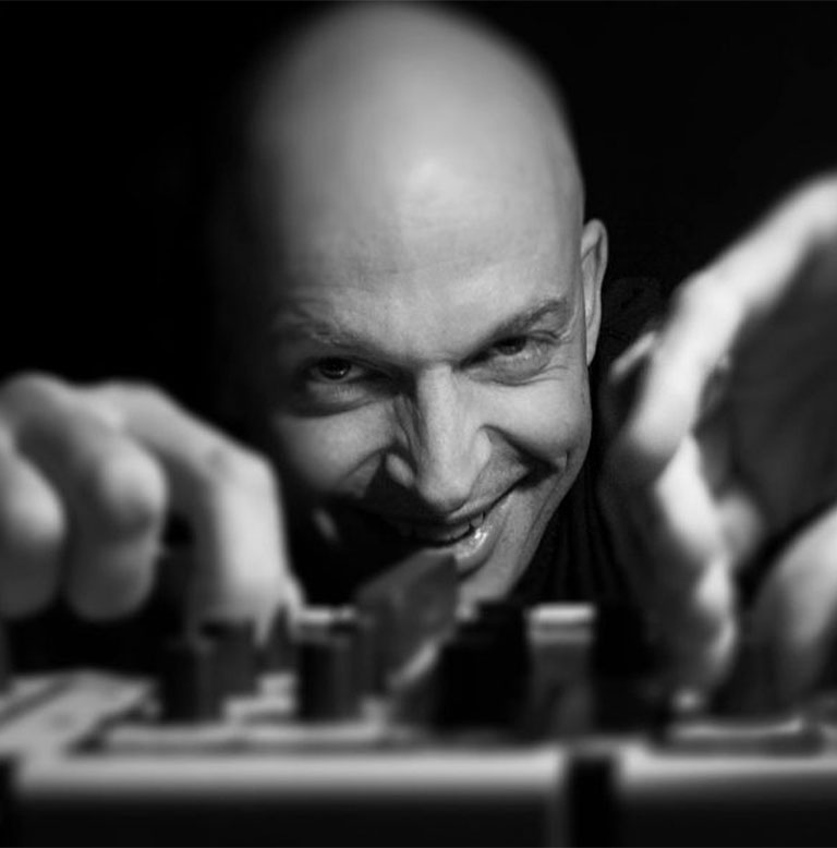 Ein DJ mit Glatze lächelt, während er an einem Mischpult arbeitet.