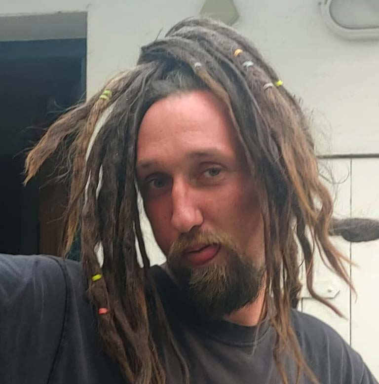 Mann mit Dreadlocks und Bart, der in die Kamera schaut.