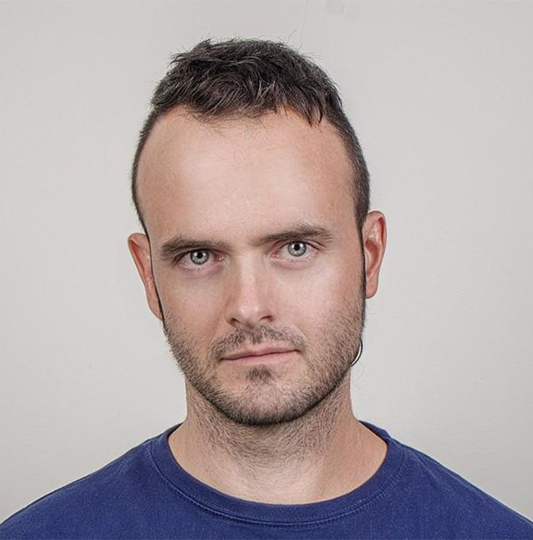 Porträt eines Mannes mit kurzem Haar und neutralem Gesichtsausdruck vor einem hellen Hintergrund.