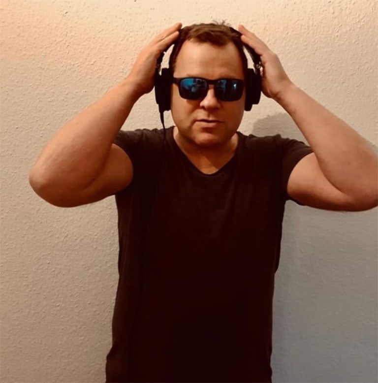 Mann trägt schwarze Kopfhörer und Sonnenbrille, während er die Hände an den Kopf legt.