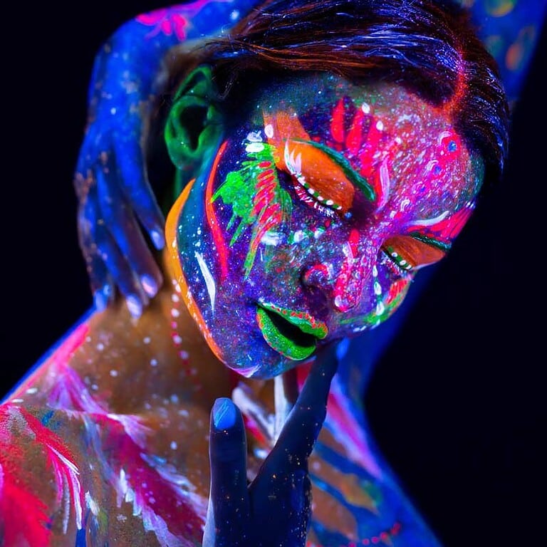 Eine Person mit leuchtender Körperbemalung in Neonfarben, die im Dunkeln strahlt.