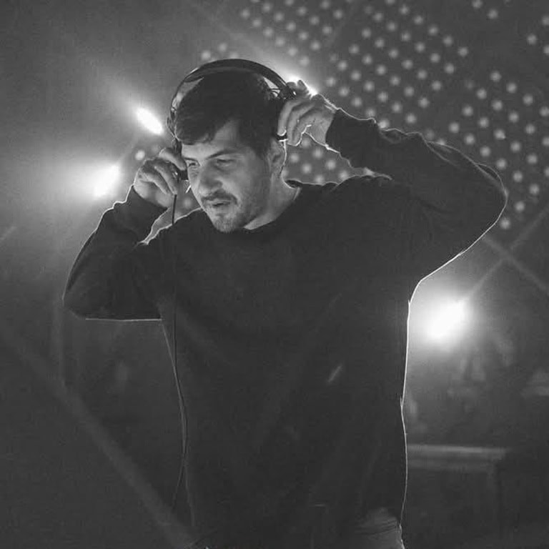 Mann mit Kopfhörern, der in einem dunklen Raum Musik auflegt, umgeben von Lichtquellen.