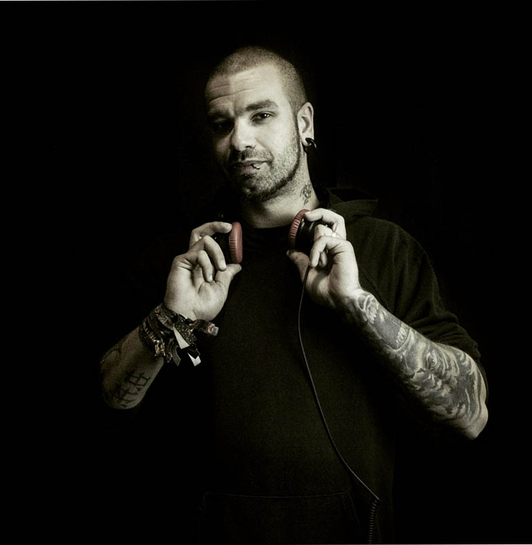 Mann mit Tätowierungen, der Kopfhörer in den Händen hält und in die Kamera schaut.