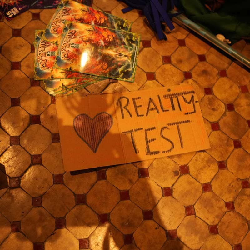Ein handgeschriebenes Schild aus Pappe mit der Aufschrift 'REALITY-TEST' auf einem gefliesten Boden.